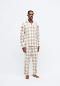 Pyžamový set s kockovaným vzorom v béžových a svetlohnedých odtieňoch. Vyrobený z mäkkej látky; obsahuje zapínanie na gombíky na vrchnej časti a dlhé nohavice s rovnými nohami.