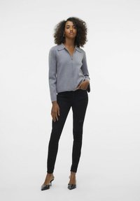 Šedá zipová mikina s jemnou texturou, dlouhými rukávy a límcem, kombinovaná s černými slim-fit džíny a černými lodičkami.