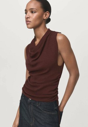 Haut sans manches bordeaux avec un col drapé et des ruchés sur les côtés, fabriqué dans un tissu doux, associé à un jean en denim foncé.