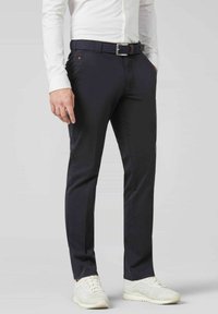 Pantalon navy en mélange de coton, présentant une coupe slim, des poches latérales et une ceinture tissée. Associé à des baskets blanches.