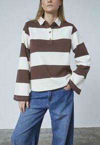 Brun og hvid stribet langærmet polo shirt med krave, knaplukning og afslappet pasform, parret med blå denim brede bukser.