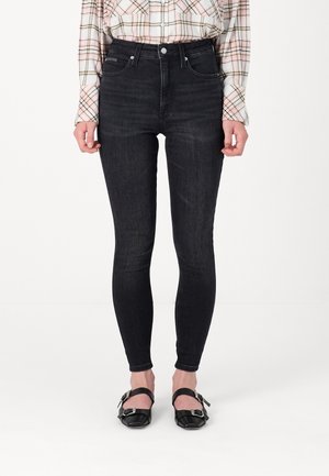 Slim fit sorte jeans båret med en lyserød ternet skjorte med knapper og sorte flade sko med sølvspænder.