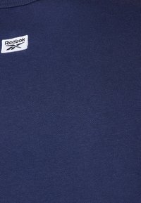 Mörkblå bomullströja med en liten vit Reebok-logotyp. Tyget har en slät yta med fin ribbing.