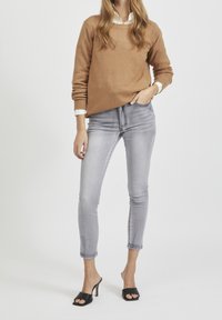 Brun tröja, ljusgrå skinny jeans och svarta öppna klackar. Tröjan har rund hals och ribbade ärmar. Släta texturer genom hela plagget.