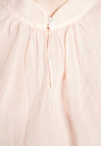 Blusa rosa chiaro con colletto rotondo, chiusura con bottoni e tessuto arricciato sullo scollo. Realizzata in un materiale morbido e leggero.
