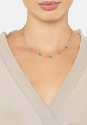 Gold chain necklace with alternating blue and clear circular gemstones, featuring a delicate design, displayed on bare skin.