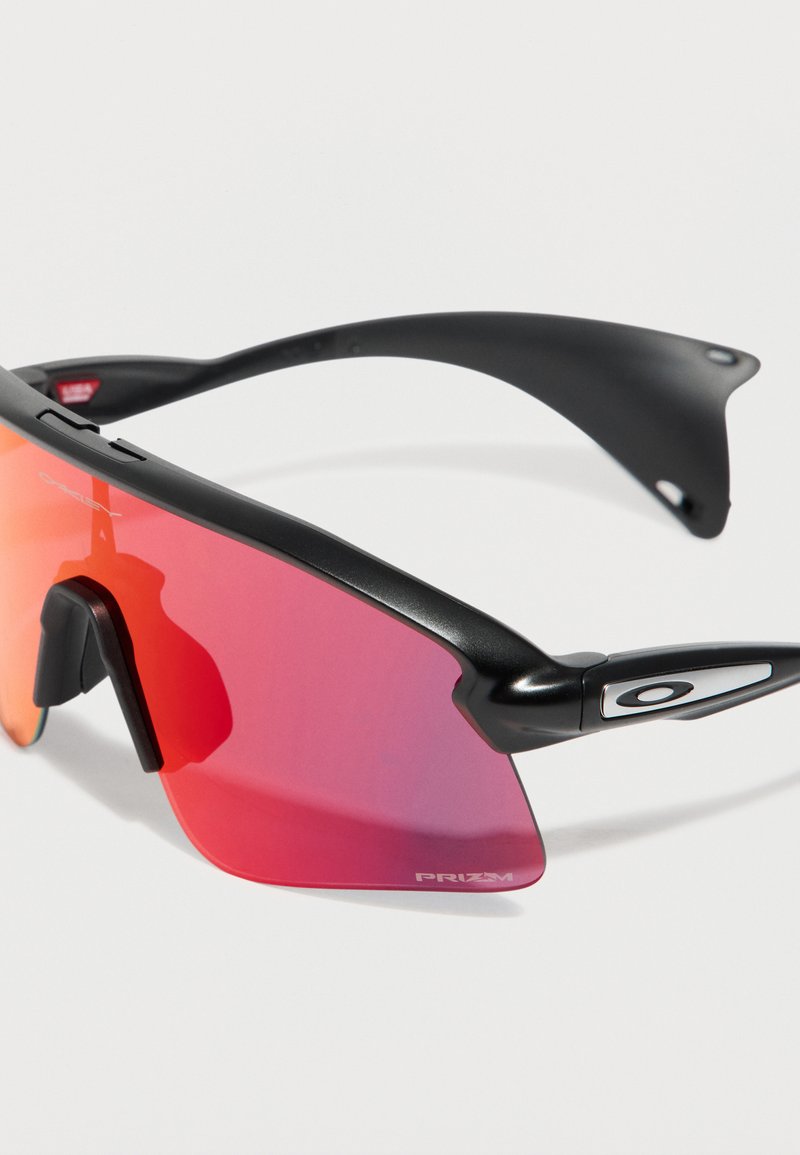 Lunettes de sport noires avec verres miroirs rouges enveloppants et logo Oakley sur la branche et le coin du verre.