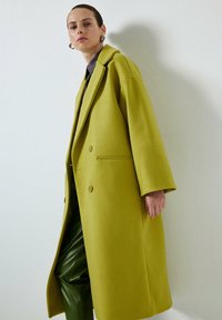 Manteau double boutonnage en vert citron vif, fabriqué en laine douce, avec une coupe décontractée, de grands revers et deux boutons à l'avant.