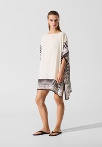 Bijeli kaftan s crnim prugastim uzorkom i ukrašenim rubom. Labav kroj s kratkim rukavima, izrađen od mekog, laganog tkanja.