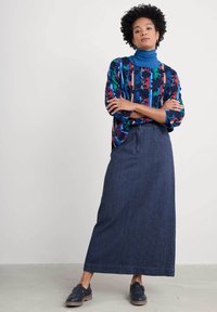 Bunt gemusterte Bluse mit hohem Kragen und lockerer Passform, kombiniert mit einem langen Dunkelblau-Denim-Rock im geraden Schnitt und mit seitlichen Taschen.