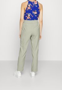 Kwiatowy top na ramiączkach w niebieskim kolorze z wielokolorowymi kwiatami, zestawiony z jasnoszarymi spodniami. Białe sneakersy dopełniają całość.