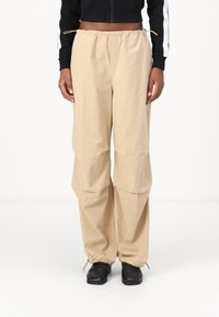 Beige, loose-fitting trousers with an elastic waist, cinched ankles, crafted from lightweight fabric. Paired with black shoes.