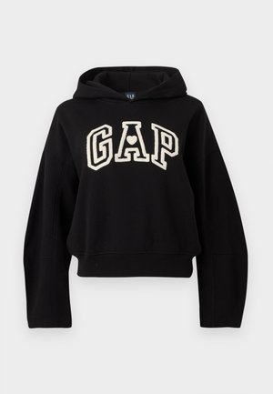 Sudadera corta negra con mangas extragrandes y un logo blanco de "GAP" que presenta un corazón dentro de la letra A en el pecho.