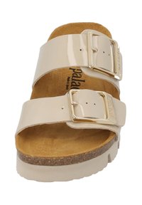 Sandali in pelle verniciata beige con due fibbie regolabili, sottopiede in sughero e una fodera interna marrone texturizzata. Suola piatta con bordi arrotondati.