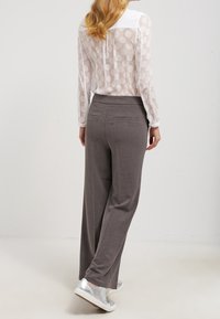 Chemise légère et transparente à manches longues avec col blanc et motif à pois ; associée à un pantalon gris à jambes larges et des baskets argentées.