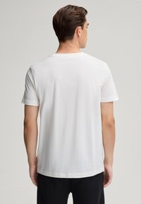 Biała bawełniana koszulka z krótkim rękawem i okrągłym dekoltem. Gładka tekstura, luźny krój. Mała metka marki widoczna z boku.