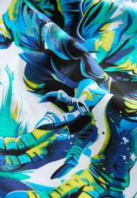 Färgglad tyg med ett livfullt blått, grönt och gult abstrakt mönster med en textur som ser slät och något glansig ut.