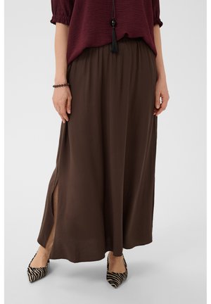 Femme portant un top bordeaux et un pantalon large marron avec des fentes sur les côtés, accessoirisée avec des chaussures pointues à motif zèbre et un collier pendentif noir.