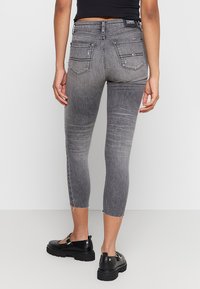 Jeans de mezclilla gris de cintura alta con una silueta ajustada, dobladillos desgastados y dos bolsillos traseros. Combinados con zapatos de plataforma negros.