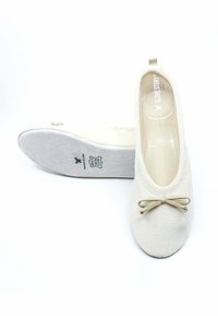 Ballerines couleur crème avec un dessus doux et texturé, bout rond et un petit nœud en accent. Semelle flexible avec une marque sur la semelle intérieure.