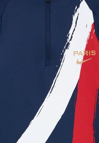 Laivastonsininen vetoketjullinen paita, jossa on suuria punaisia ja valkoisia siveltimenvetoja, sekä kultaiset "PARIS"-teksti ja Nike-logo. Sujuvaa, joustavaa kangasta.