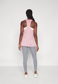Top deportivo rosa con diseño de espalda nadador, sobre un sujetador deportivo blanco, combinado con leggings ajustados grises y zapatillas deportivas blancas.