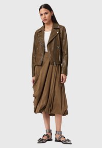 Giubbotto da biker in pelle marrone con zip silver, abbinato a una gonna fluida marrone e sandali con tacco silver, posizionato su uno sfondo neutro.