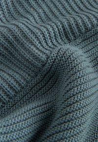 Gros plan d'un tissu tricoté bleu-gris montrant des points côtelés et texturés avec des plis doux.