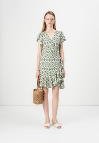 Πράσινο φόρεμα με μοτίβο και ρυάκια στα μανίκια, με φρουτώδη άκρη, συνδυασμένο με κρεμ σανδάλια και τσάντα γύρου από πλεγμένο υλικό.
