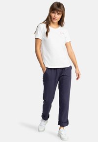 Camiseta blanca de manga corta con el logo de Roxy, combinada con pantalones tapered azul marino y zapatillas blancas, con puños enrollados y bolsillos.