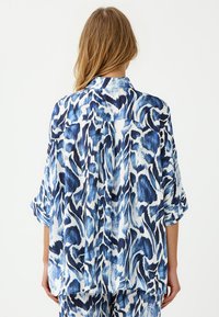Blau-weiße gemusterte Bluse mit lockeren Ärmeln, einem Kragen und einem entspannten Schnitt, aus einem leichten Stoff mit einer glatten Textur.
