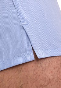 Lichtblauw visgraatpatroon stof met een detail van een gespleten zoom. Zichtbare stiksels en textuur op de stof. Close-up van shorts.