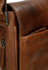Sac messager en cuir brun au toucher lisse, doté d'une poche zippée bien visible et d'un rabat carré avec un motif matelassé subtil.