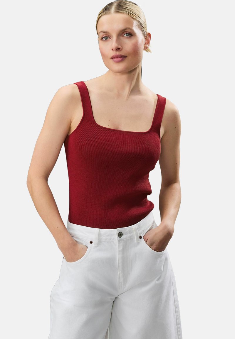 Débardeur rouge côtelé avec un décolleté carré et de larges bretelles, assorti à un pantalon blanc à taille haute avec poches latérales et fermeture à bouton.