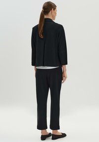 Zwart op maat gemaakte blazer met driekwartmouwen, gecombineerd met bijpassende zwarte broek. Glad materiaal met een licht gestructureerde afwerking.