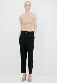 Beige ribbel zonder mouwen top met uitsparingen, gecombineerd met zwarte high-waisted broeken met een knoop aan de voorkant en zijzakken.