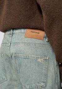 Ljusblå denimjeans med blekning, slitna detaljer och en rektangulär läderlapp i tan med texten "EIGHTYFIVE" på midjan.