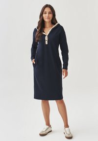 Marineblauwe lange mouwen hoodie jurk met een beige contrasterende strook, zakken en een relaxte pasvorm. Gemaakt van zacht materiaal, geschikt voor casual kleding.