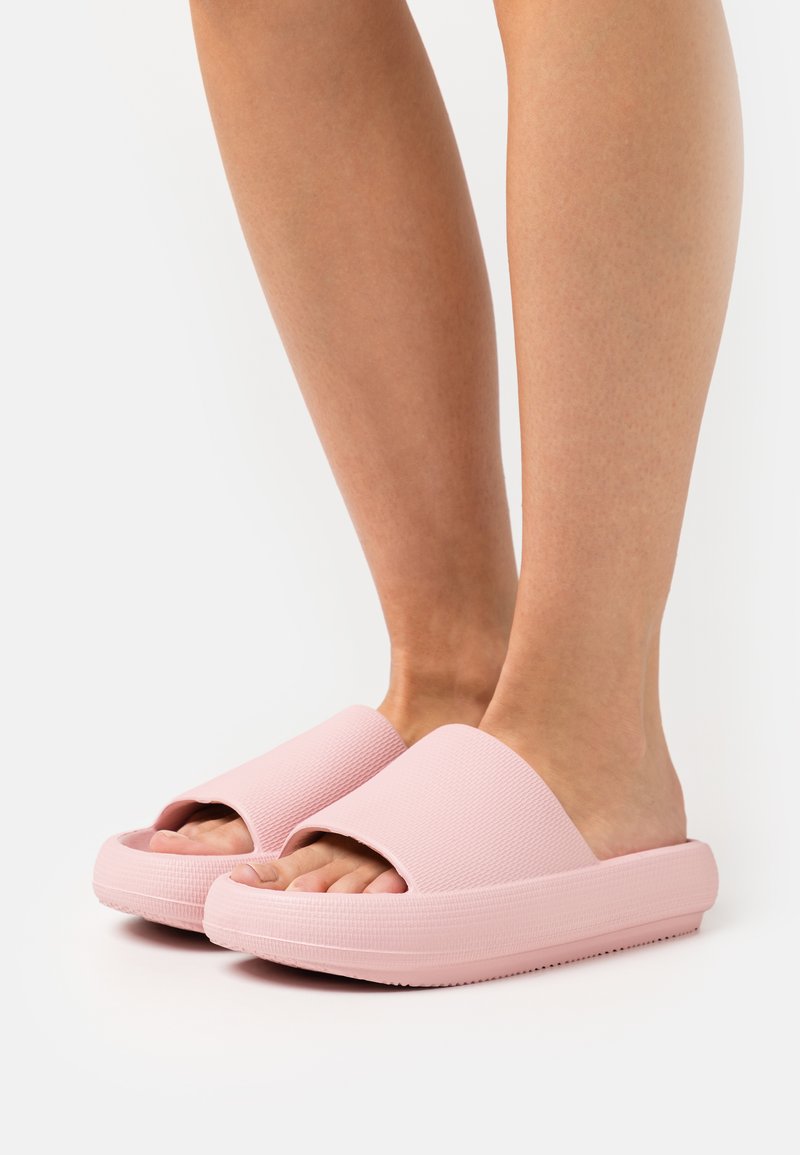 Le ciabatte rosa presentano una parte superiore testurizzata con ampie aperture, una suola spessa e una finitura liscia, offrendo un design minimalista.