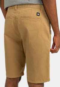 Khaki šortky vyrobené z ľahkého materiálu, s uvoľneným strihom, dvoma zadnými vreckami a malou nášivkou s logom blízko pásu.