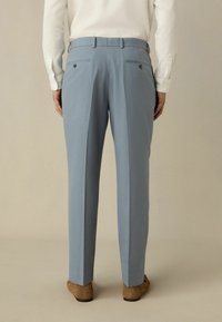 Lichtblauwe broek van gladde stof, met achterzakken met knoopsluitingen, rechte pijpen en een tailleband met riemlussen.