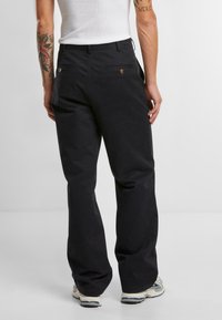 Black cotton trousers with a relaxed fit, featuring back pockets with gold hardware accents. Smooth texture, straight leg design.