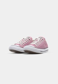 Pink canvas sneakers with white laces, rubber soles, black stripes, and a logo patch on the tongue. Smooth texture and low-top design.