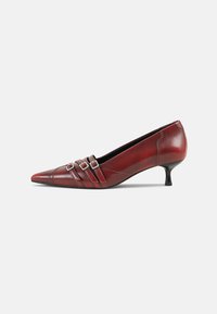 Zapato de tacón rojo de cuero con punta afilada, tacón bajo, correas horizontales y hebillas cuadradas plateadas, con detalles de costura elegantes.