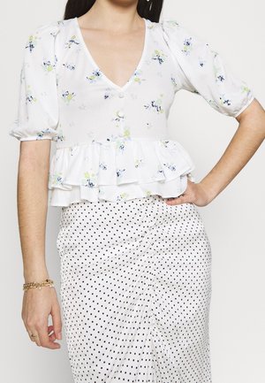Haut blanc à fleurs avec manches ballons, ourlet volanté et encolure en V. Associé à une jupe blanche à pois avec des détails de tissu froncé.
