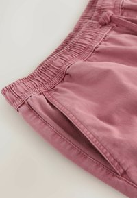 Gros plan sur un short à taille élastique rose poussiéreux avec détail de poche latérale sur un fond clair.