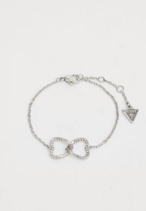 Silver bracelet featuring an infinity symbol adorned with clear rhinestones, attached to a fine chain with a clasp and a triangular tag.