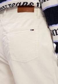 Valged kelmjeansid, tagaküljel on silt "JEANS" ja väike logo silt punases, valges ja sinises. Nähtav tekstureeritud ribaleht.