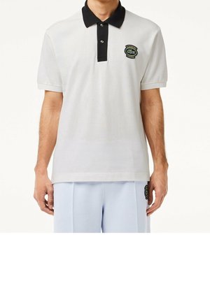 Weißes Poloshirt mit schwarzem Kragen, zwei Knöpfen und grünem gesticktem Logo auf der linken Brust. Baumwollstoff mit glatter Textur.