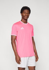 Ροζ αθλητική μπλούζα με λευκές λεπτομέρειες και λογότυπο Adidas στο αριστερό στήθος. Κοντά μανίκια και στρογγυλή λαιμόκοψη. Ελαφρύ, λείο ύφασμα.